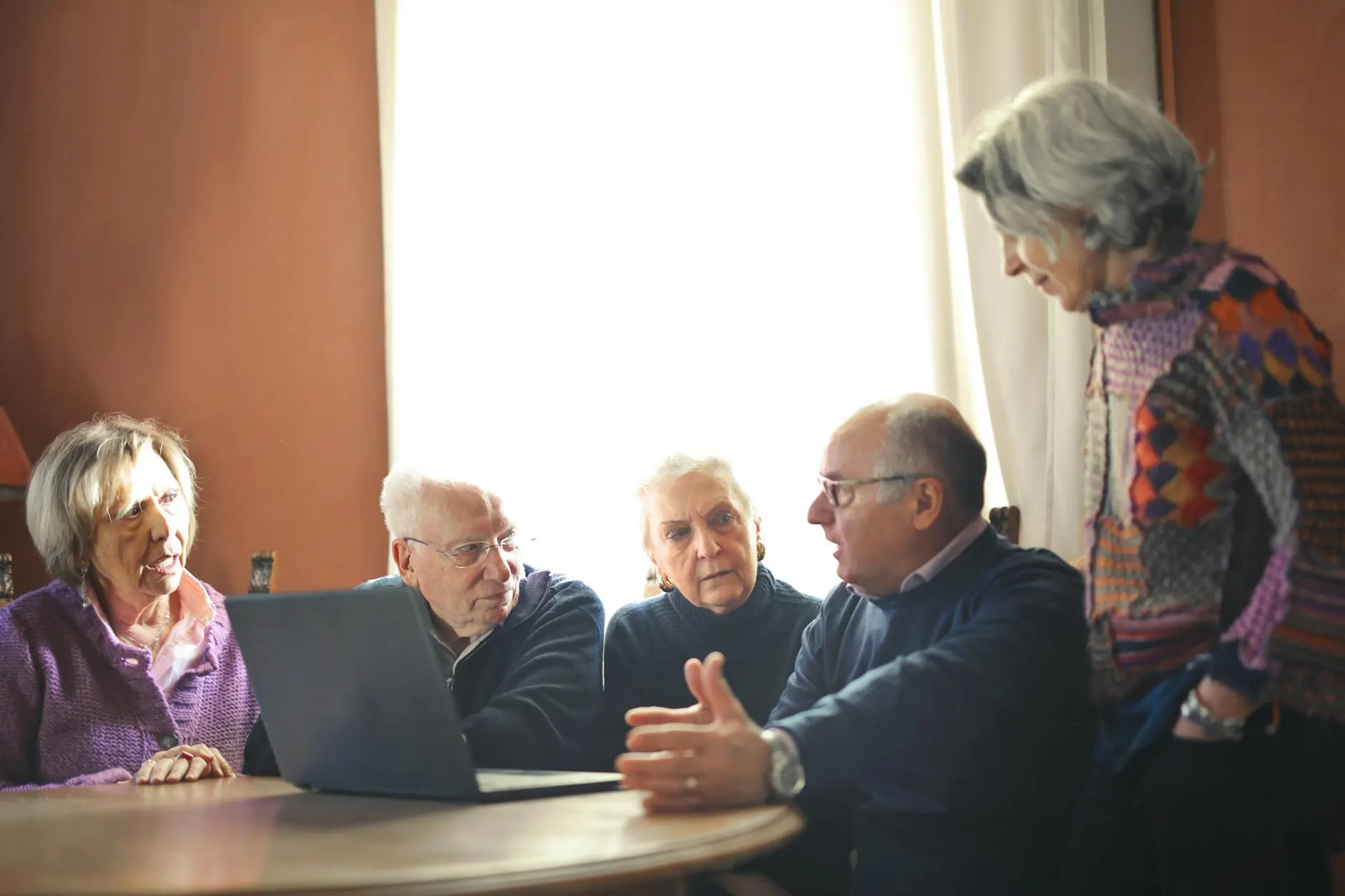 Group of senior adults discussing around a laptop in a warm indoor setting.